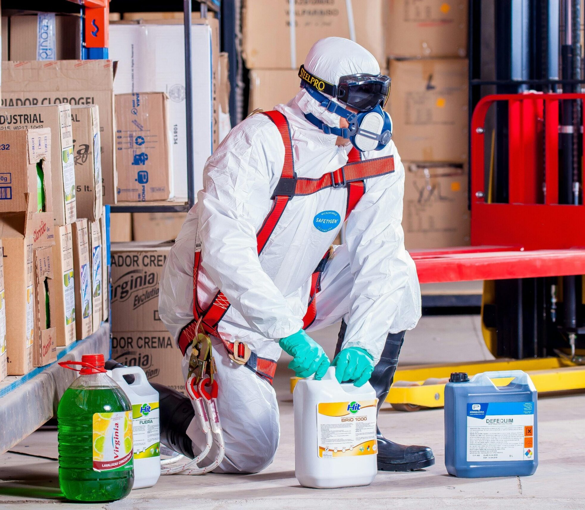 Industrial worker in protective gear handling chemicals in a warehouse environment.